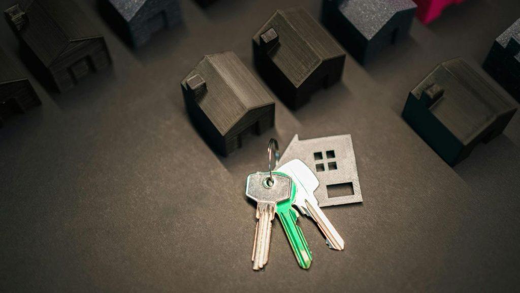 Keys on a ring with a metal house tag, placed among dark model houses on a dark surface