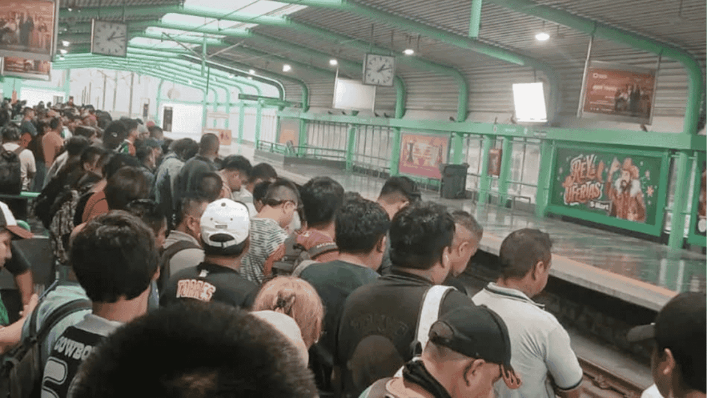 Crowded metro platform with many people standing in line along the green-tinted walls and posters.