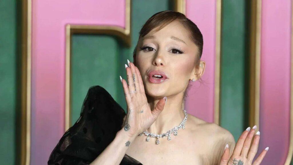 Fotografía de Ariana Grande con un vestigo negro de gala diciendo algo y poniendo su mano sobre su rostro