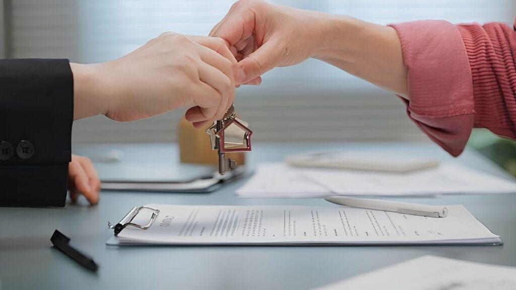 tips-de-finanzas-de-quantium-desarrollos - CLAVE NOTICIA Two people exchange a set of keys over a desk with documents, glasses, and a pen nearby.